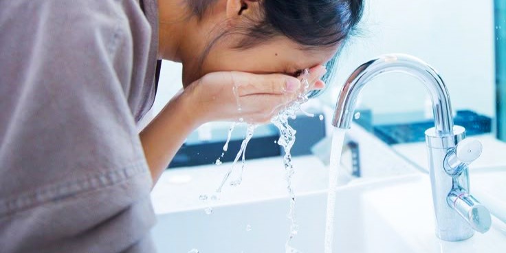 a girl splashing hot water on her face in the morning making her skin more greasy.